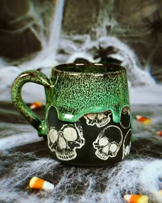 a green and black coffee mug with skulls on the inside is surrounded by candy corn