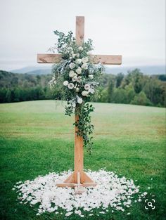 a wooden cross decorated with flowers and greenery on top of a grass covered field