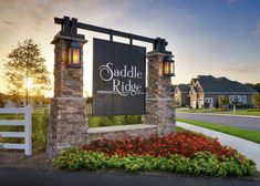 the sign for saddle ridge at sunset in front of a house with flowers and trees