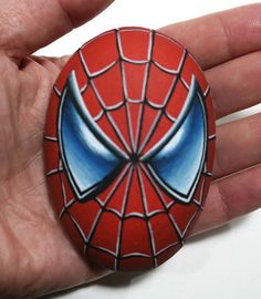 a hand holding a painted rock with a spiderman face on it's side