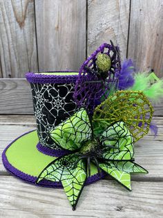 a green and black top hat with purple flowers on the side, sitting on a wooden surface