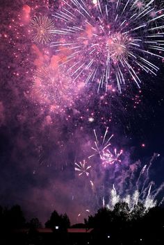 fireworks are lit up in the night sky above some trees and buildings with lights on them