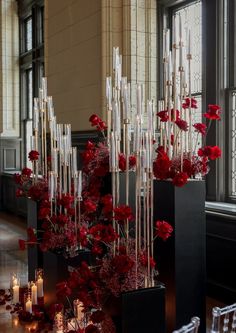 red flowers and candles are arranged in black vases on the floor near large windows