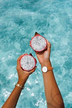 two people holding fruit in their hands near the water