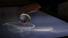 a person touching a glass ball on top of a table with white powder sprinkles