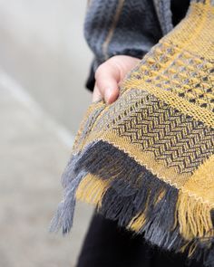 a person holding a yellow and black shawl with fringes on it's ends