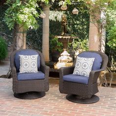 two wicker chairs sitting on top of a brick patio next to a water fountain