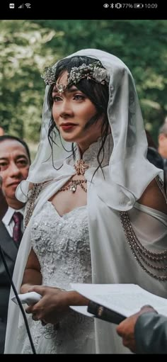 a woman in a white wedding dress and veil holding a piece of paper while standing next to other people