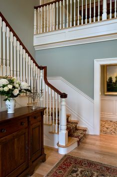 a vase with flowers sitting on top of a wooden table next to a stair case