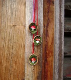 three ornaments are hanging on the side of a wooden door with red ribbon and mushrooms