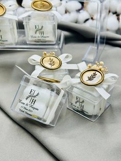 four small clear boxes with gold and white decorations on top of a cloth covered table