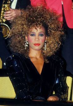 a woman with curly hair sitting in front of a man holding a saxophone and wearing red lipstick