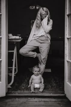 a woman standing next to a baby on top of a door way with her leg up in the air