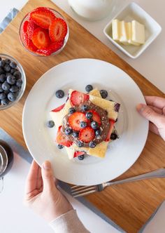 a person is holding a plate with pancakes and berries on it next to some fruit