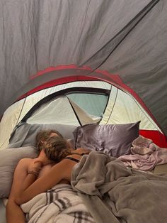 a woman laying in bed with her head on the pillow next to a sleeping bag