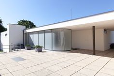 an outdoor room with glass walls and potted plants on the outside wall, in front of a white building