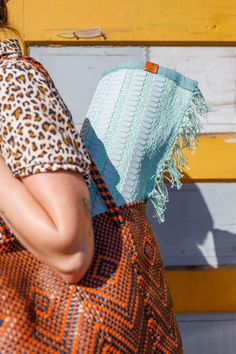 a woman carrying an orange and black purse on her shoulder with a leopard print top