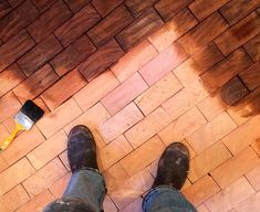 a person standing on top of a wooden floor next to a paint can and brush