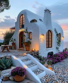 a house made out of rocks with plants and flowers in the front yard at dusk