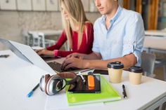 two people sitting at a table with laptops and coffee cups in front of them