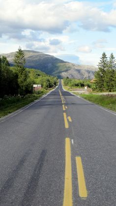 an empty road with yellow painted lines on both sides and mountains in the distance behind it