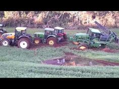 four tractors are parked in the middle of a field with mud puddles on it