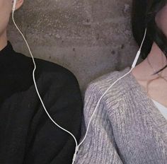 two people with ear buds on their ears, one is listening to the other's headphones