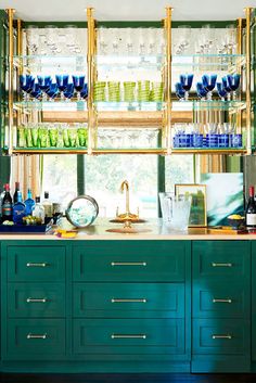 a kitchen filled with lots of bottles and glasses on top of a green cabinet next to a window