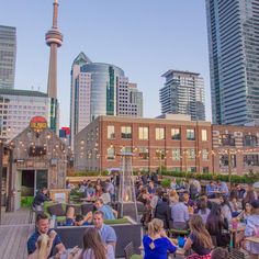 a group of people sitting at tables on top of a roof in front of tall buildings