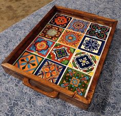 an old wooden box with colorful tiles on the top and bottom, sitting on a blue patterned tablecloth