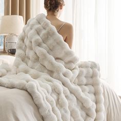 a woman sitting on a bed under a fluffy white blanket with her back turned to the camera