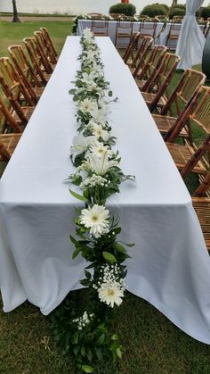 a long table with white flowers and greenery on the top is set up for an outdoor event