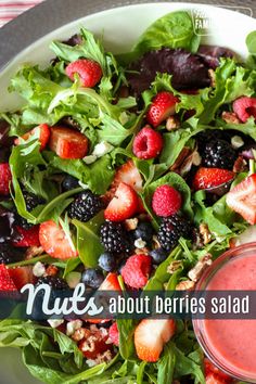 a salad with berries and nuts is on a plate next to a small bowl of dressing