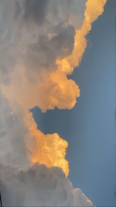 an airplane flying in the sky with some clouds behind it and yellow light coming from below