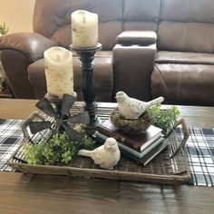 a tray with candles, books and birds on it in front of a leather couch