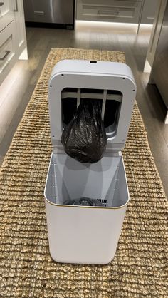 a white box with a black bag in it sitting on a rug next to an oven