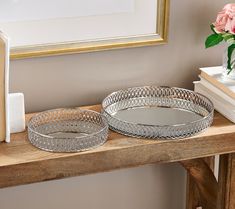 two metal trays sitting on top of a wooden table next to a vase with flowers