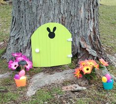 a green door with ears on it next to some flowers and potted plants in front of a tree