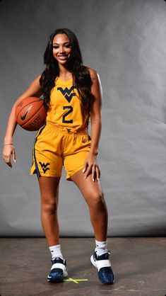 a woman in a yellow uniform holding a basketball and posing for the camera with her hands on her hips