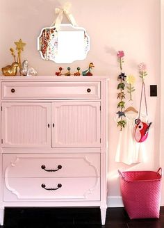 a pink dresser in the corner of a room next to a white door and mirror