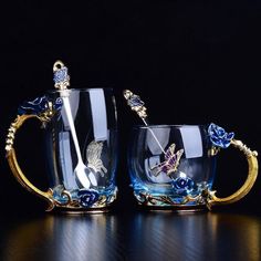 two glass mugs with spoons in them sitting on a table next to each other