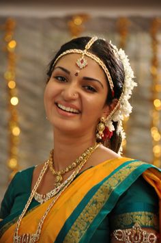 a woman in a yellow and green sari with jewelry on her head, smiling at the camera