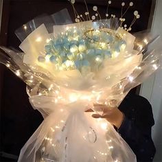 a person holding a large bouquet of flowers with lights on it's stems and wrapped in clear cellophane