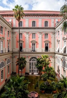 an old pink building with palm trees in the courtyard and potted plants on the ground