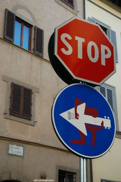 two street signs on top of each other in front of a building with shuttered windows