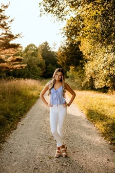 a beautiful young woman standing on a dirt road