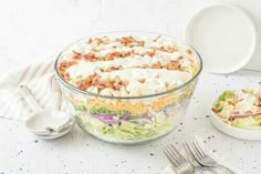 a salad in a bowl with dressing on the side next to a plate and fork