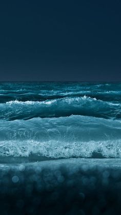 an ocean with waves crashing on the shore and dark blue sky in the back ground