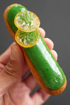 a person is holding a tiny green pastry with lemon slices and limes on it