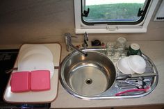 a kitchen sink with dishes and utensils next to the window in an rv